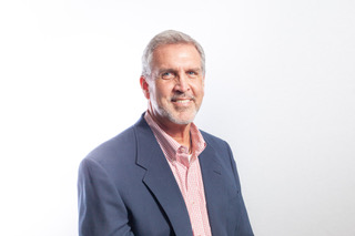 Middle-aged man in blue blazer and pink checkered shirt smiling Middle-aged man with gray hair and beard wearing blue blazer and pink checkered shirt on white background